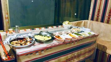 A dining table set with various dishes, a window with curtains, and a patterned tablecloth.