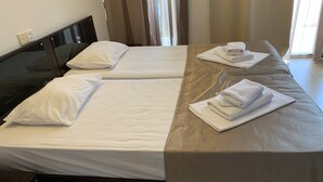Et hotelværelse med to senge, begge med hvide hør og puder, et træsengegærde og et bord med sammenfoldede håndklæder.