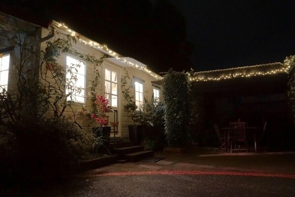 A building with multiple windows, a covered patio area, and string lights. - Cosy Cottage in Central Paihia (Paihia)