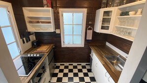 A compact kitchen with a black and white checkered floor, wooden cabinets, and a window with a view.