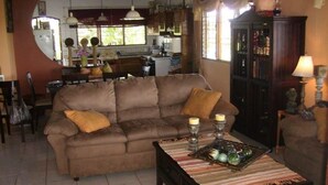 Una sala de estar acogedora con un sofá marrón, una mesa de centro con objetos decorativos y una cocina al fondo.