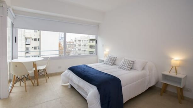 A modern bedroom with a bed, bedside tables, a small table with chairs, and a large window. - TPYN Palermo (Buenos Aires)