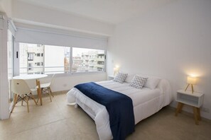 A modern bedroom with a bed, bedside tables, a small table with chairs, and a large window.
