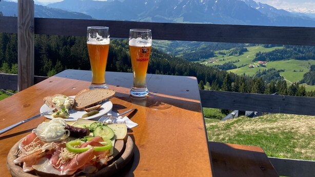 A table with a meal and two glasses of beer, overlooking a mountainous landscape. - "schossbach" Baubiologische Ferienwohnung 60 qm, Zwei Extra Schlafzimmer (Aschau im Chiemgau)