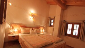 A cozy bedroom with a wooden bed, a nightstand, and a window with curtains. - "schossbach" Baubiologische Ferienwohnung 60 qm, Zwei Extra Schlafzimmer (Aschau im Chiemgau)