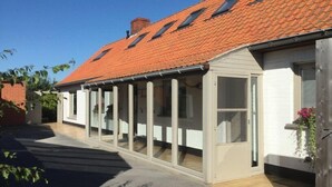 A single-story house with a red-tiled roof, a covered porch with glass doors, and a small garden area with a flower pot. - holiday home for 10 people (Oostvleteren)