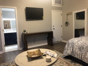 A bedroom with a bed, a TV mounted on the wall, a bedside table, and a small round table with a basket and a remote control. - Casa Indigo -- Cozy & Chic in GREAT LOCATION! (San Antonio)