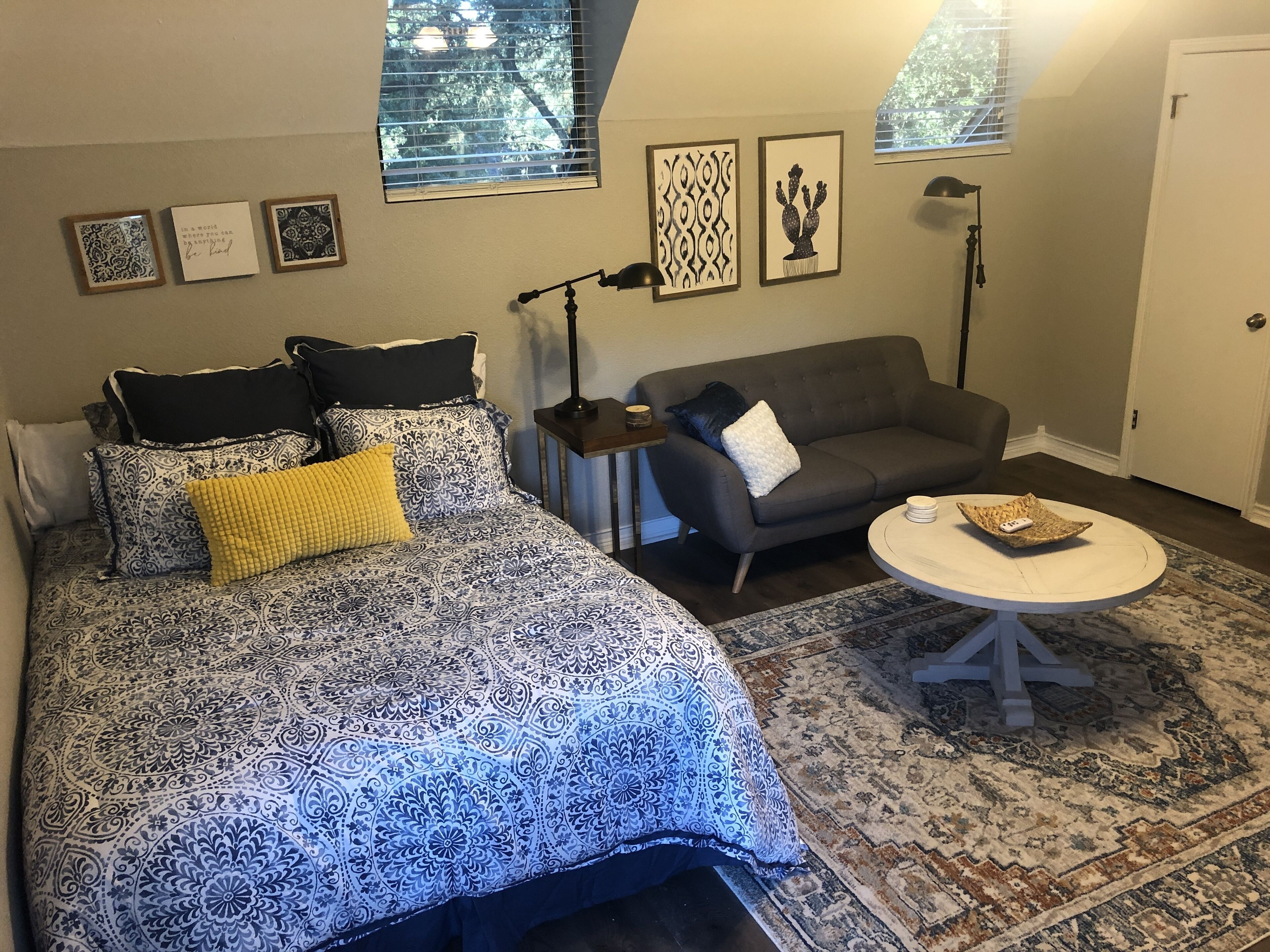 Um quarto com cama, sofá cinza, mesinha e tapete estampado.