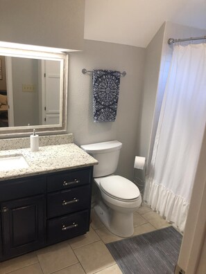 A bathroom with a white sink, dark cabinets, a toilet, and a shower curtain. - Casa Indigo -- Cozy & Chic in GREAT LOCATION! (San Antonio)