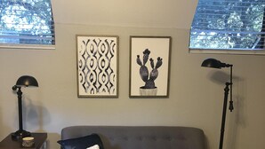 A living room with a grey sofa, a round coffee table, a lamp, and two framed artworks on the wall. - Casa Indigo -- Cozy & Chic in GREAT LOCATION! (San Antonio)