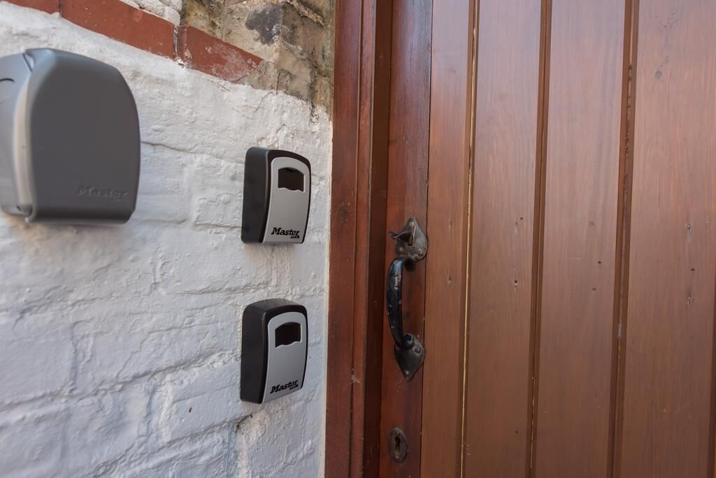 Een houten deur met een metalen handvat en twee deurbellen met de tekst 'Mastery', bevestigd aan een witte bakstenen muur.