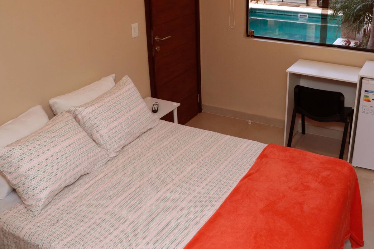 A bedroom with a bed, a desk, and a window overlooking a pool.