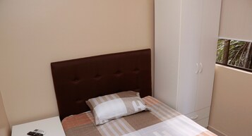 Ein Schlafzimmer mit einem Bett, einem Nachttisch, einem Kleiderschrank und einem Fenster mit Blick auf Palmen.