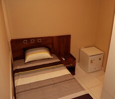 Una habitación de hotel pequeña con una cama individual, una mesita de noche y un armario blanco.