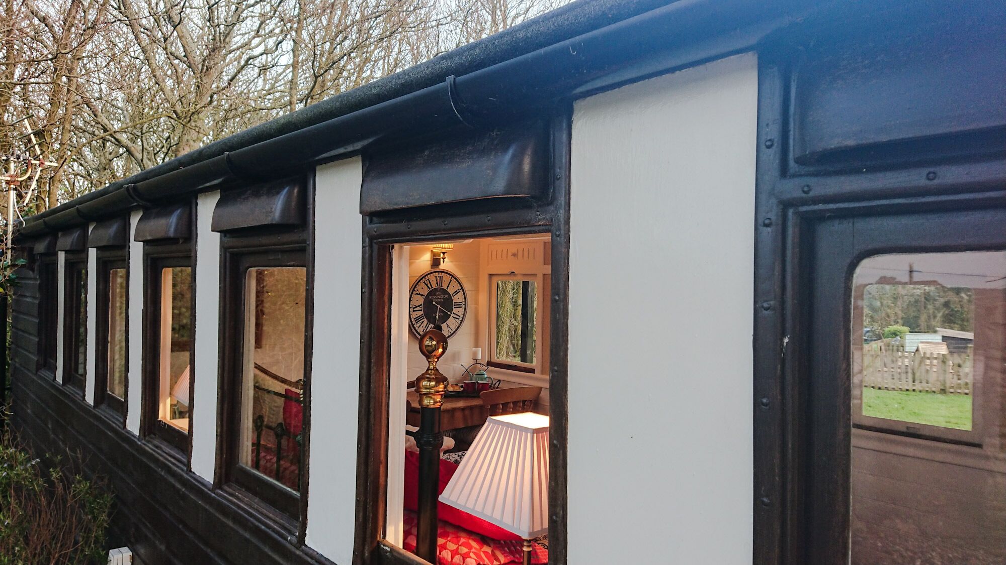 A train carriage with a clock, a lamp, and a window with a view of a garden.