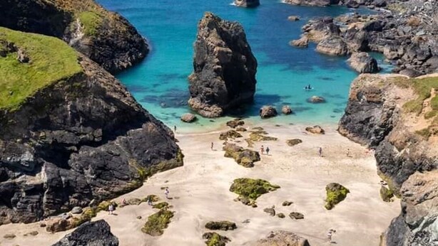 Un paysage côtier caractérisé par un terrain rocheux, des eaux turquoise et limpides, et une plage de sable.