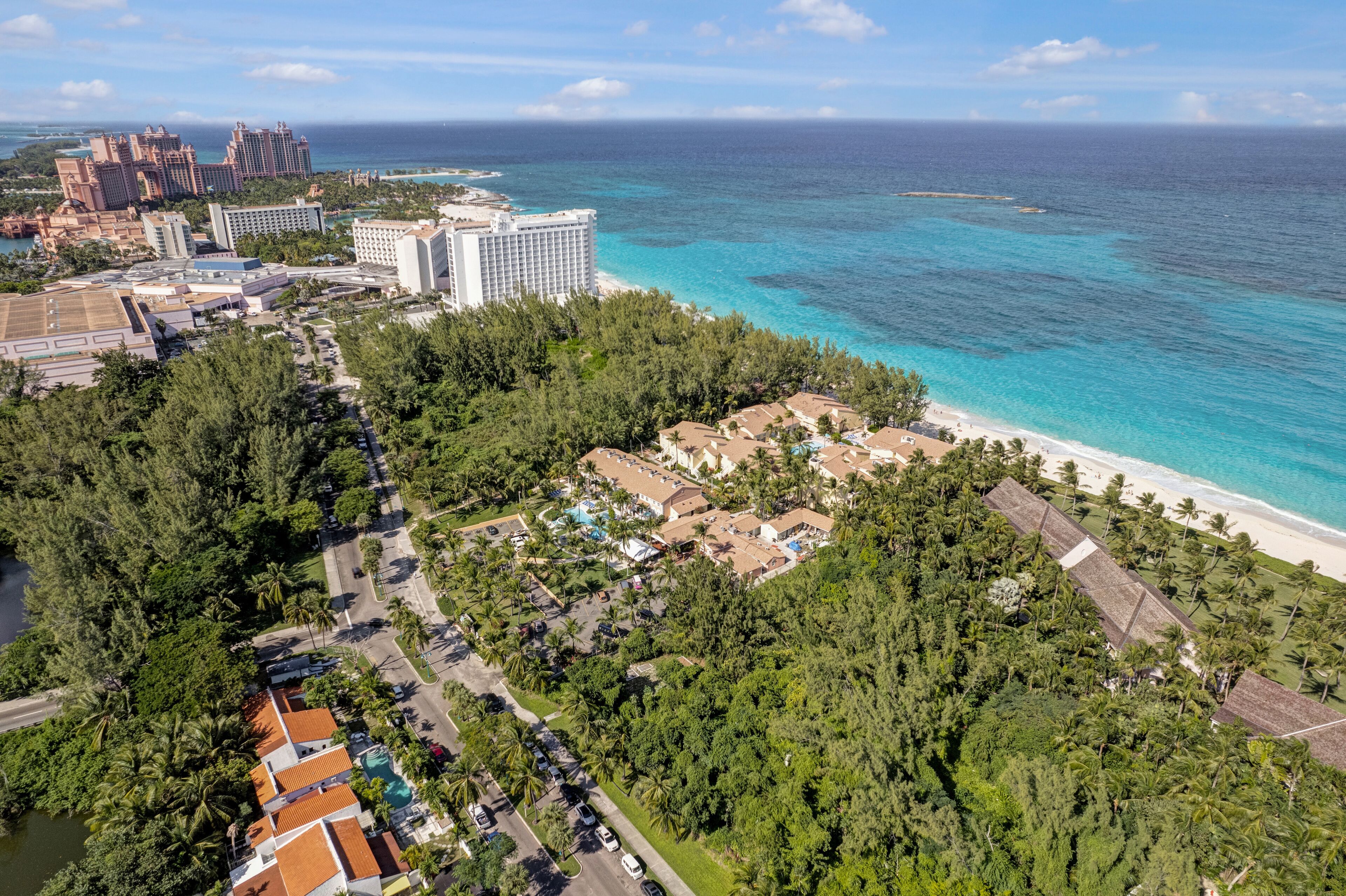 An aerial view of a coastal resort with a beachfront, dense greenery, and several high-rise buildings.