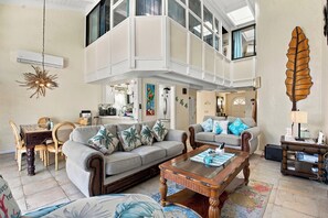 A spacious living area with a high ceiling, a dining set, and a cozy seating arrangement.