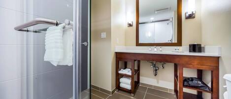 Un baño moderno con cabina de ducha de vidrio, tocador de madera con espejo y retrete.