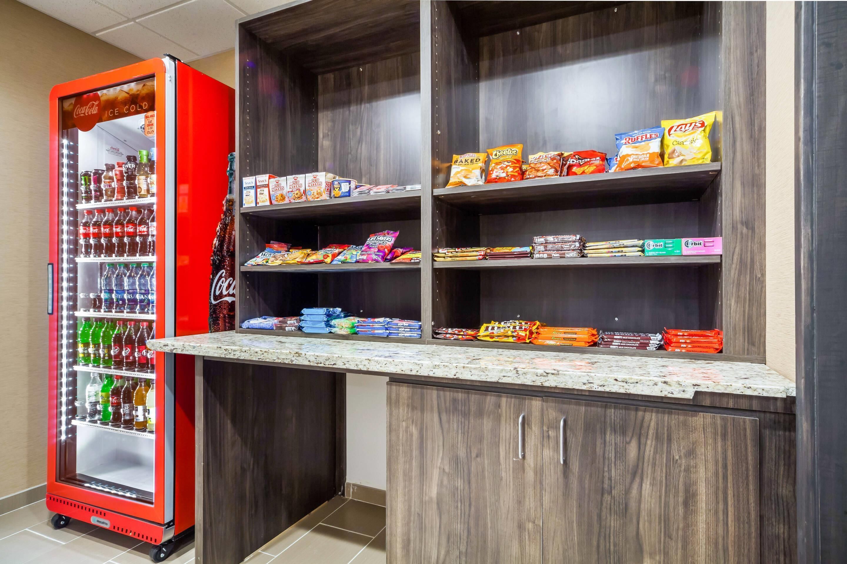 A vending machine stocked with beverages and snacks, a countertop with packaged goods, and wooden shelving units.