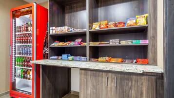 A vending machine stocked with beverages and snacks, a countertop with packaged goods, and wooden shelving units.