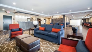 A spacious lobby with a blue sofa, red armchairs, and a brown ottoman. There is a reception desk in the background and a large wall with a textured pattern.