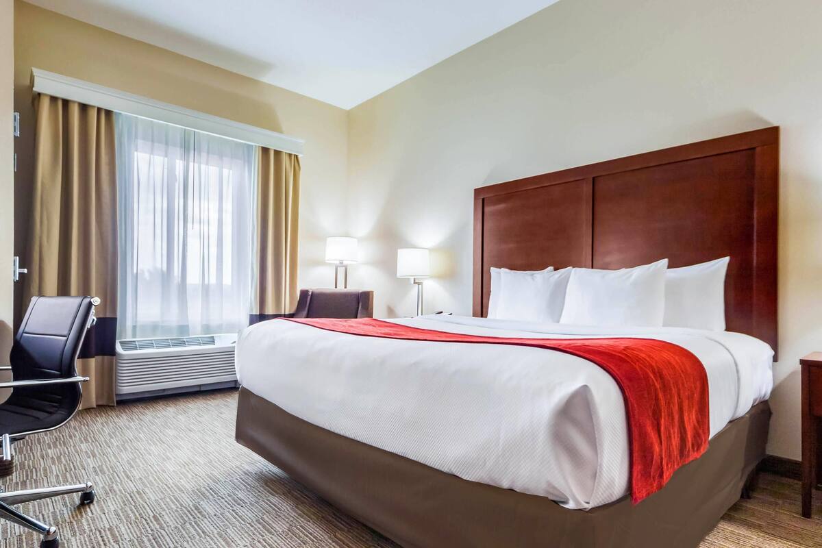 Habitación de hotel con una cama grande, una silla, un escritorio y una ventana con cortinas.