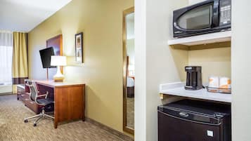 Habitación de hotel con escritorio, silla, televisión y un área de kitchenette con microondas y refrigerador.