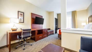 A hotel room with a desk, chair, TV, and a bed.