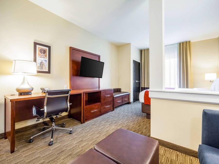 A hotel room with a desk, chair, TV, and a bed.