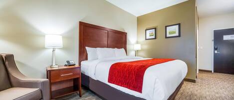 A hotel room with a large bed, a nightstand with a lamp, a chair, and a door.