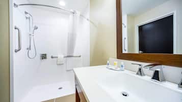 Un baño moderno con ducha, barras de apoyo, lavamanos con espejo y un perchero para toallas.