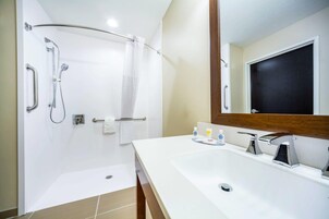 Un baño moderno con ducha, barras de apoyo, lavamanos con espejo y un perchero para toallas.