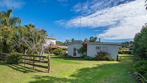 A single-story house with a small front yard, a wooden fence, and a clear blue sky. - Matapouri Beach Family Haven - Matapouri Home (Matapouri)