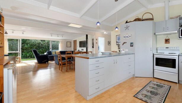 A modern kitchen with a central island, white cabinetry, and a view of the outdoors. - Matapouri Beach Family Haven - Matapouri Home (Matapouri)