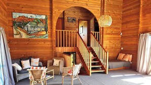 Un interno accogliente con una scala in legno, un divano, due poltrone in vimini e un quadro appeso al muro.