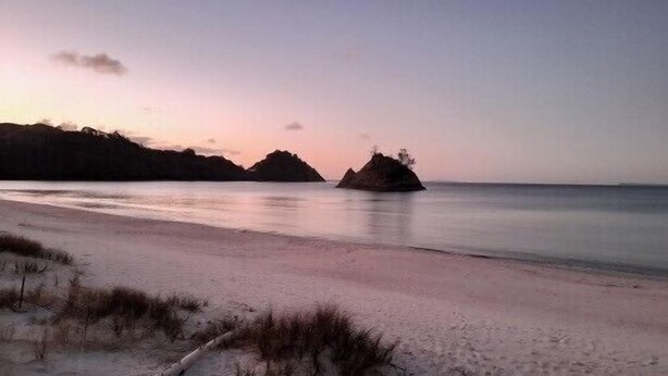 Una spiaggia con acque calme e due formazioni rocciose ben visibili all'orizzonte.
