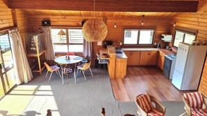 Un accogliente interno di una baita con arredamento in legno, una zona pranzo con sedie, una cucina con elettrodomestici e una vista attraverso ampie finestre.