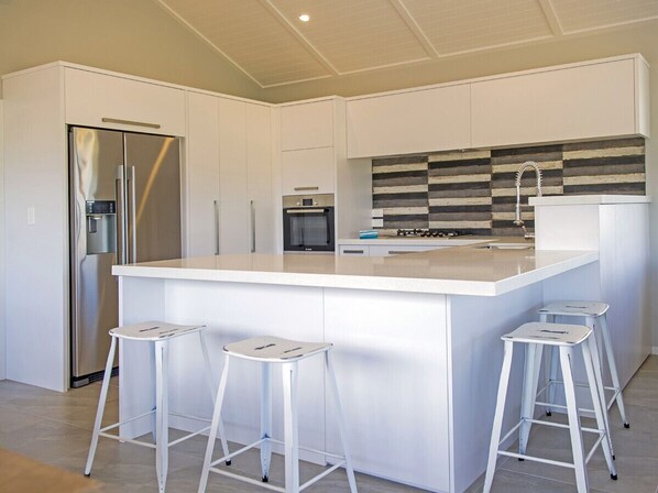 Una cocina moderna con una isla central, electrodomésticos de acero inoxidable y taburetes blancos.