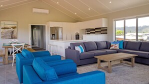 A modern living room with blue sofas, a wooden coffee table, and a kitchen area in the background.