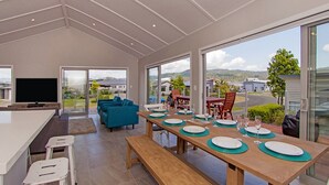 A modern kitchen with a dining area, large windows, and a view of the surrounding landscape.