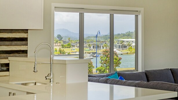 A modern kitchen with a large window, a built-in sink, and a view of a marina and mountains.
