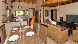 A spacious living area with a dining table set for four, a sofa, a TV, and a kitchen area with a window.