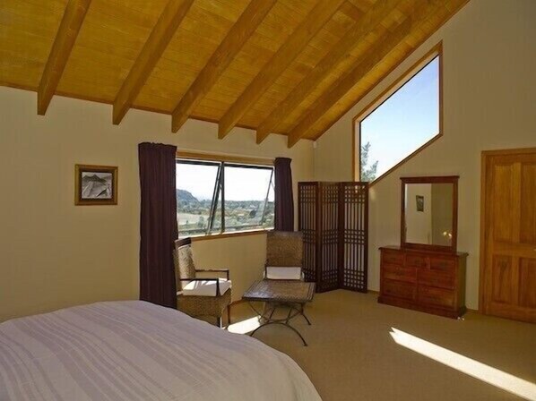 A bedroom with a large bed, a chair, a dresser, and a window with a view of the outdoors.