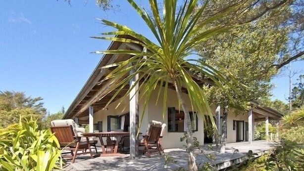 A house with a patio area, outdoor furniture, and a large tree in the foreground.