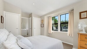 A bedroom with a bed, a dresser, a window with curtains, and a fan.