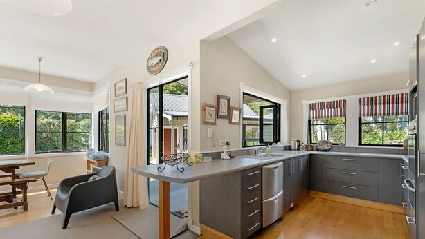 A modern kitchen with a large island, grey cabinets, and a view of greenery outside.