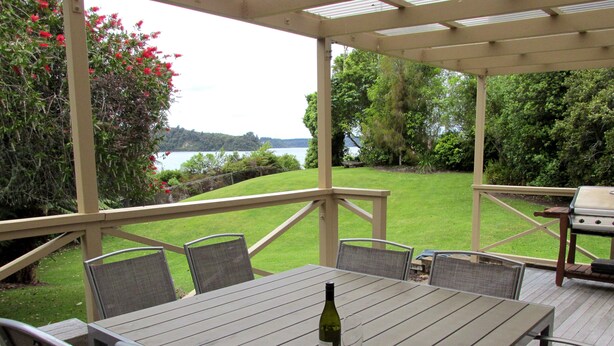 An outdoor patio with a table and chairs, a grill, and a view of a lake and greenery.