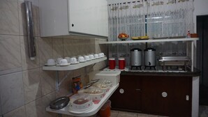 A kitchen with white cabinets, a stainless steel refrigerator, and a countertop with a coffee maker, kettle, and food containers. - Pousada Orquidário (Santos)