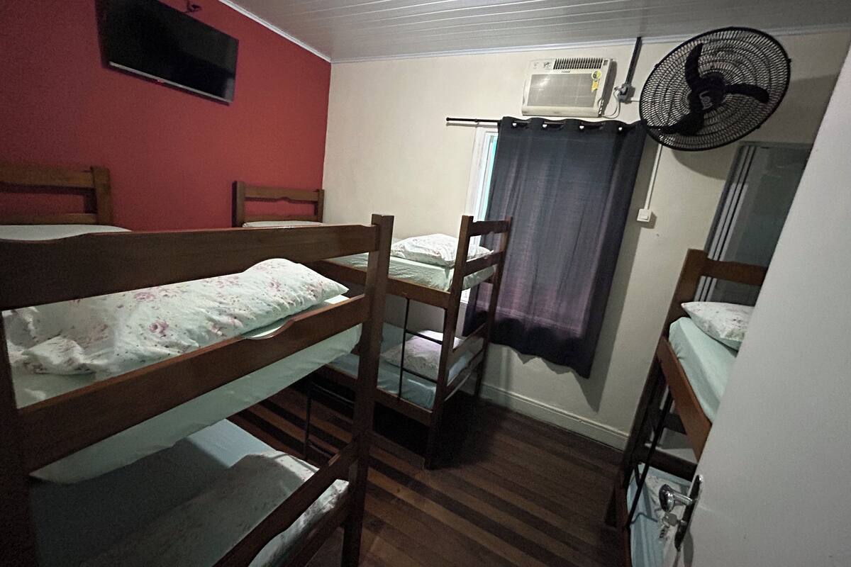 Un dormitorio con literas, ventilador de techo, unidad de aire acondicionado y televisor montado en la pared.